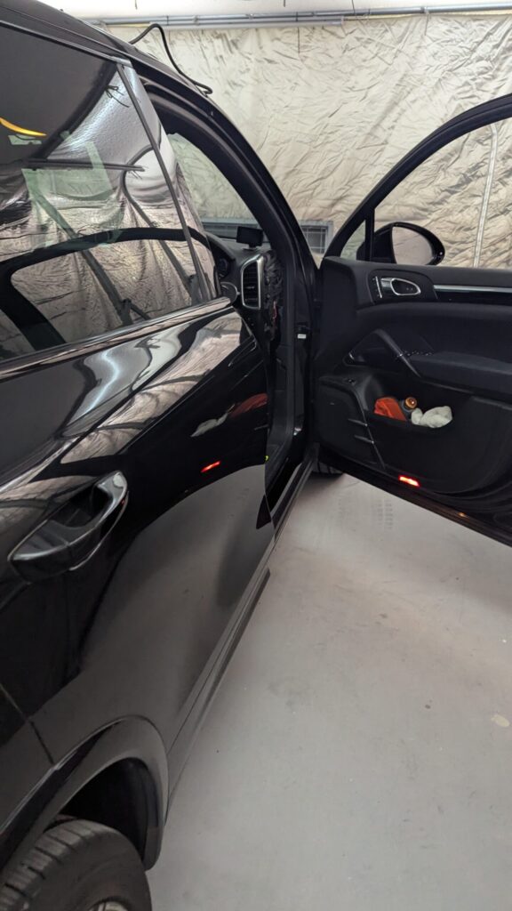 Black SUV with both front and rear passenger doors open, parked in a garage with a light-colored backdrop.