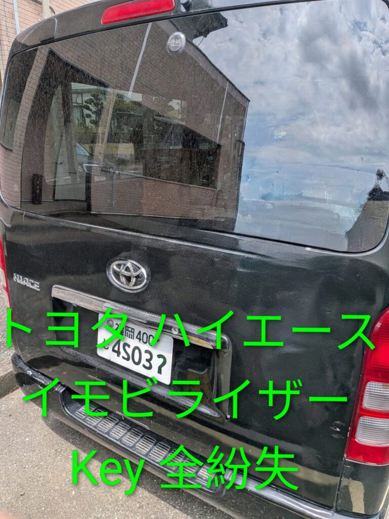 Rear view of a black Toyota Hiace van with a license plate visible; neon green Japanese text overlays the image.