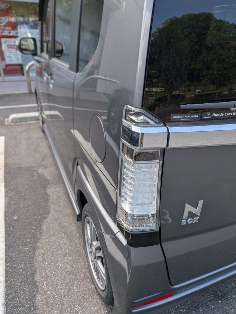 グレーのホンダN-BOXのリアコーナーのクローズアップ。縦型のテールランプとクロームのトリムが見える。